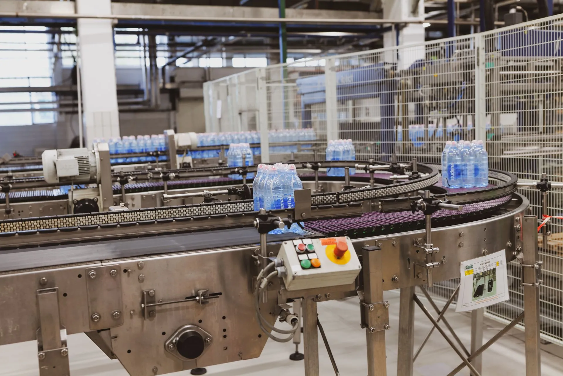 Produktionslinie mit Förderbändern und Flaschengebinden in einer Industriehalle.